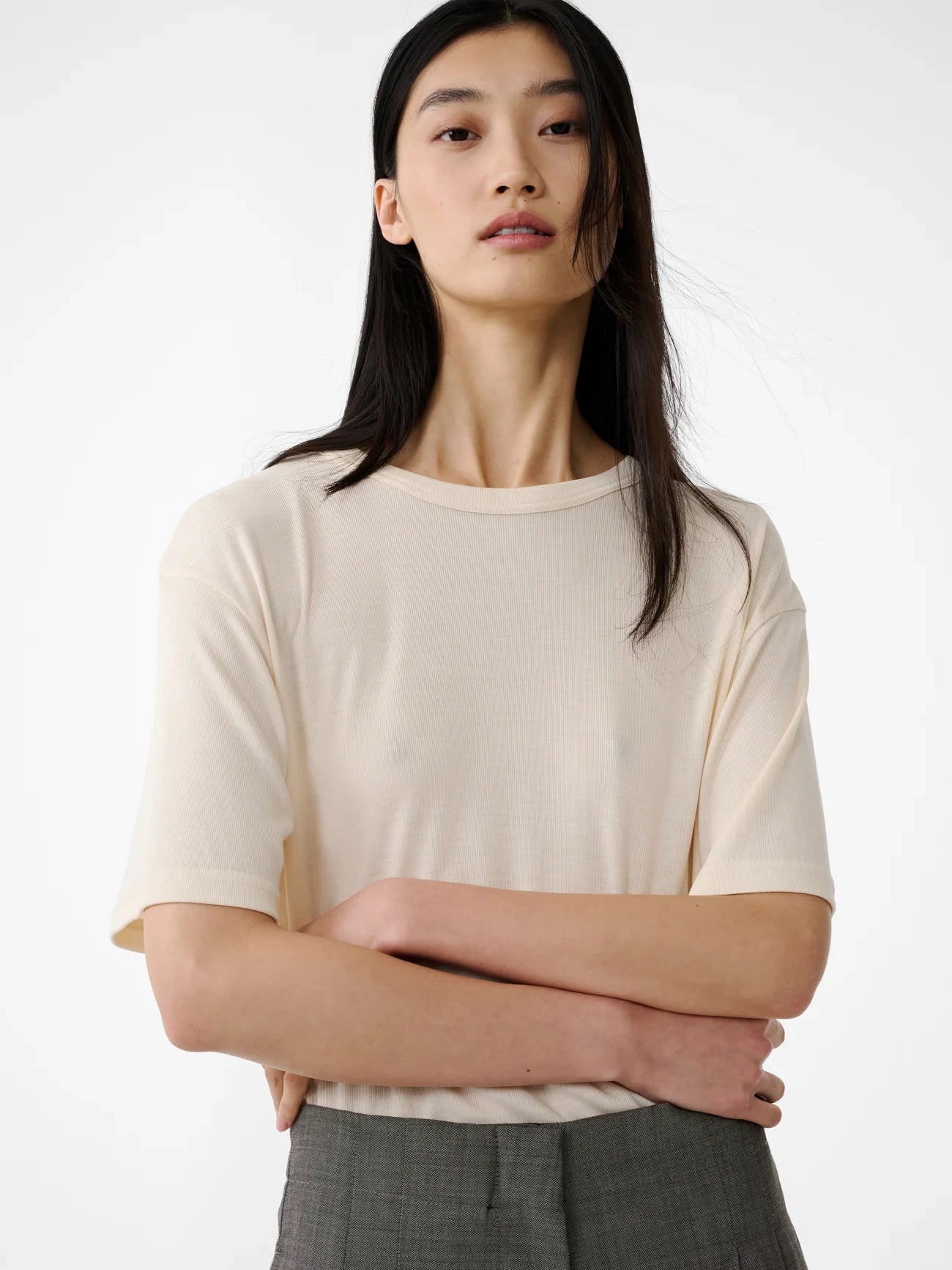Person wearing a beige top with crossed arms on a white background