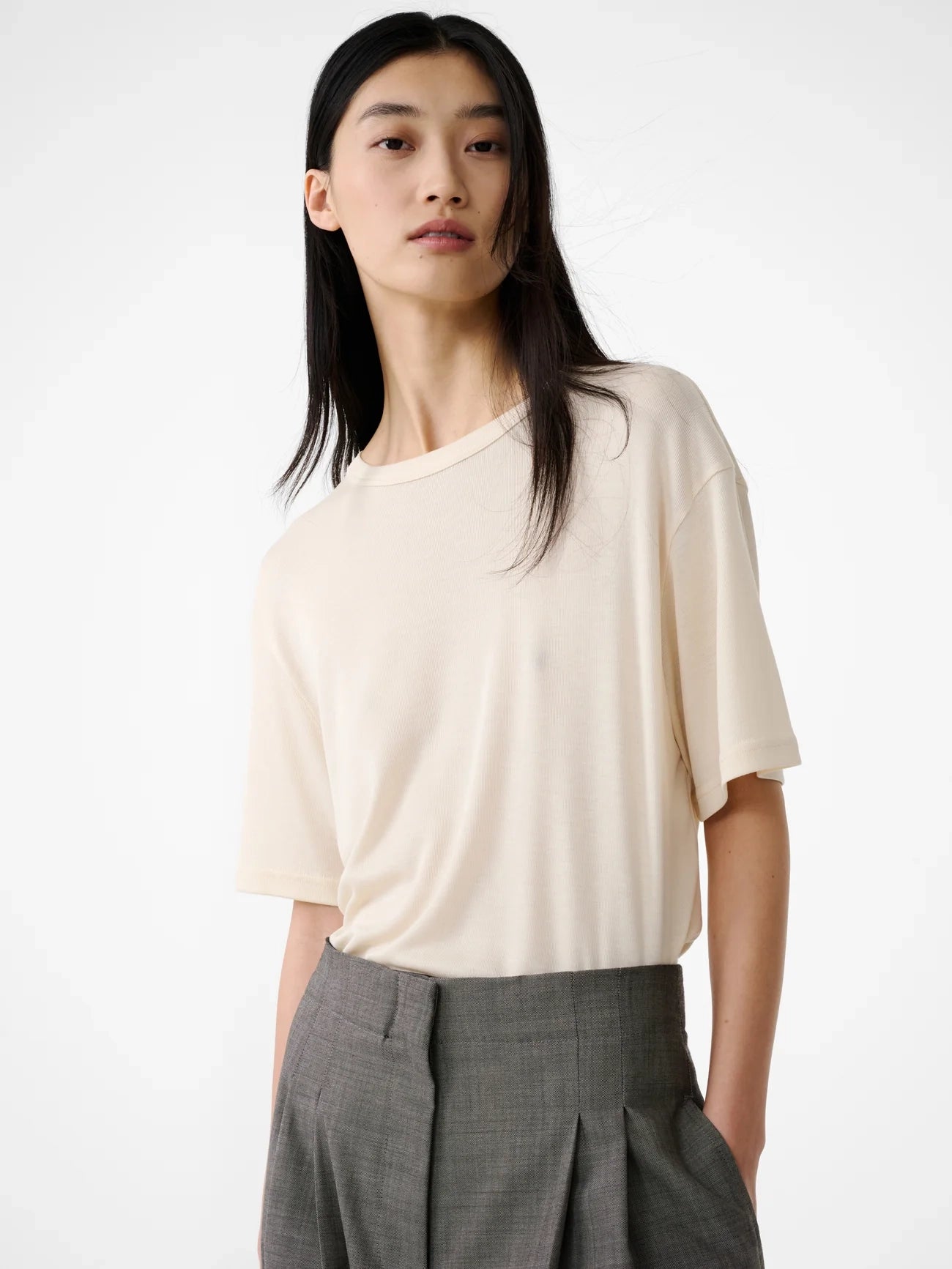 Person wearing a beige top and gray pants on a white background