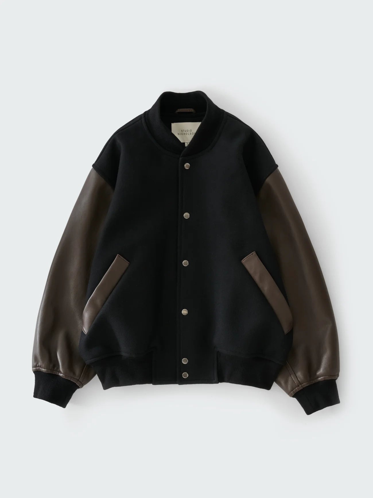 Black varsity jacket with brown leather sleeves on a white background