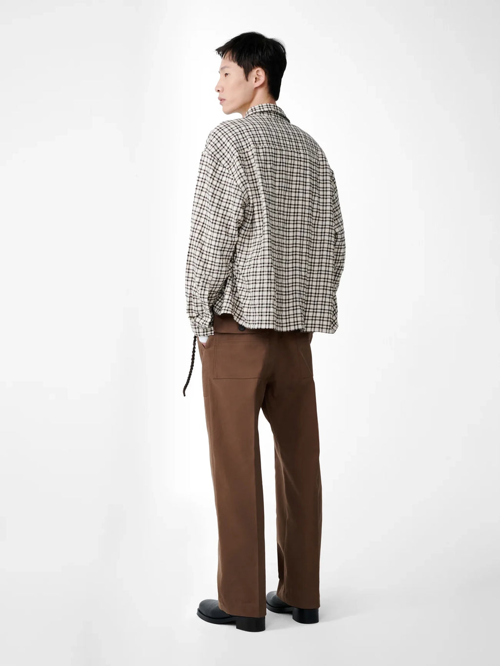 Person wearing a checkered shirt and brown pants on a white background