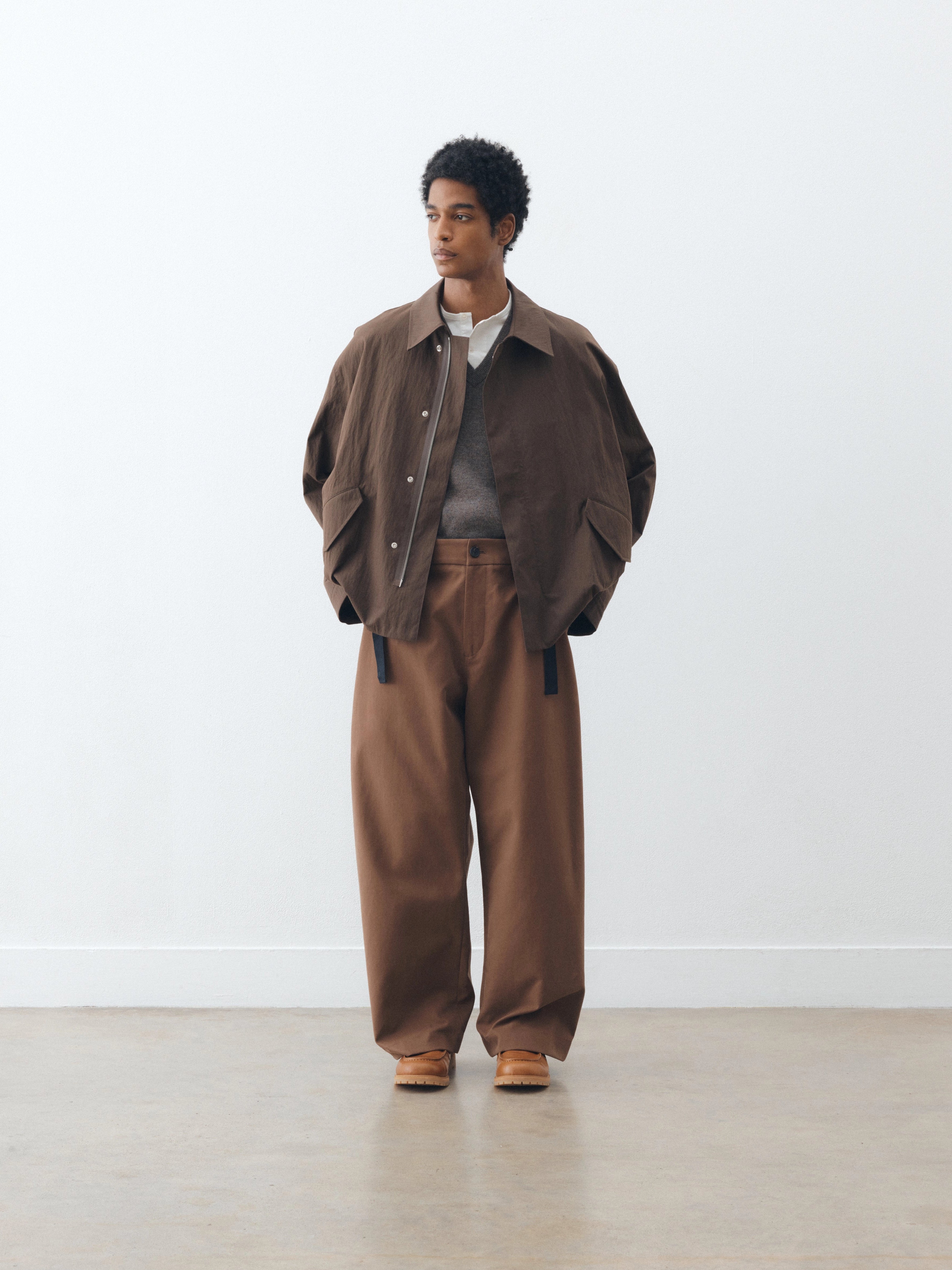 Studio Nicholson Balos pant in capucin with a wide, voluminous leg and relaxed fit, worn with a cropped jacket and layered knit, full length with clean drape.