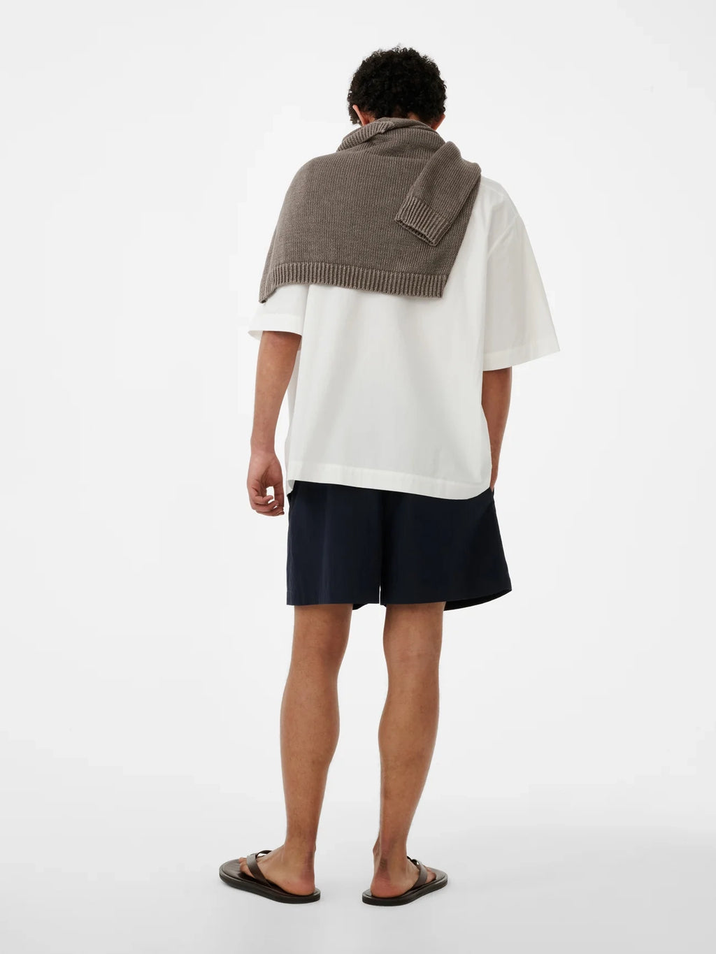 Person wearing a white shirt, navy shorts, and a brown knitted shawl on a white background
