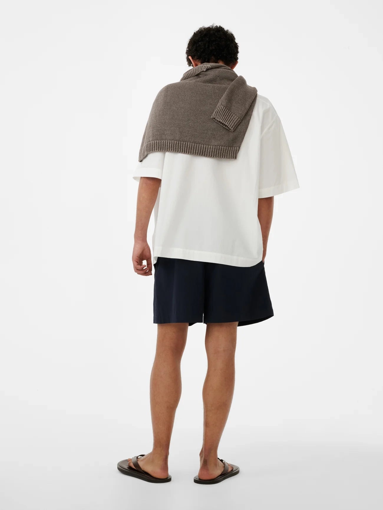 Person wearing a white shirt, navy shorts, and a brown knitted shawl on a white background