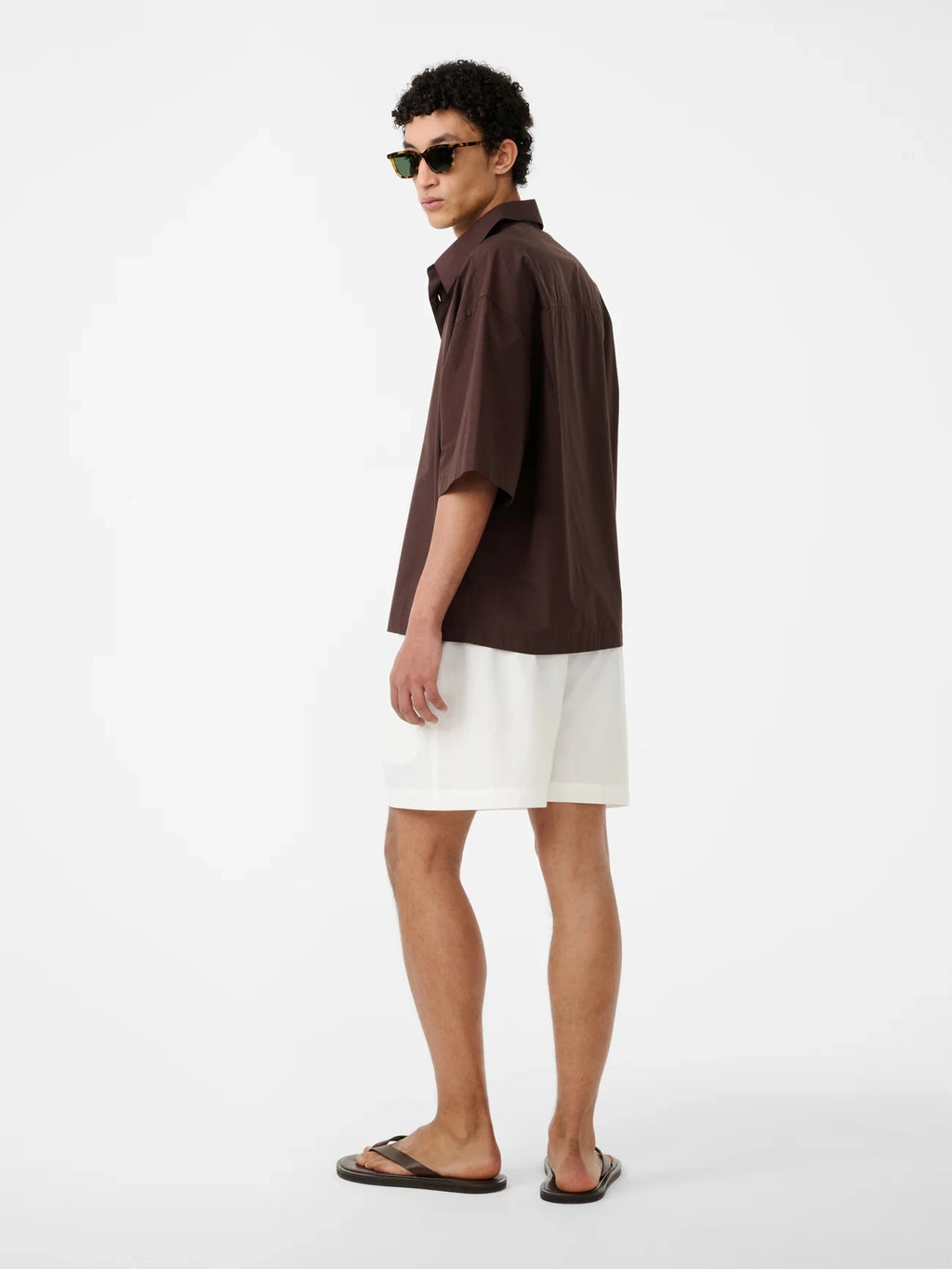 Man wearing a brown shirt and white shorts on a white background