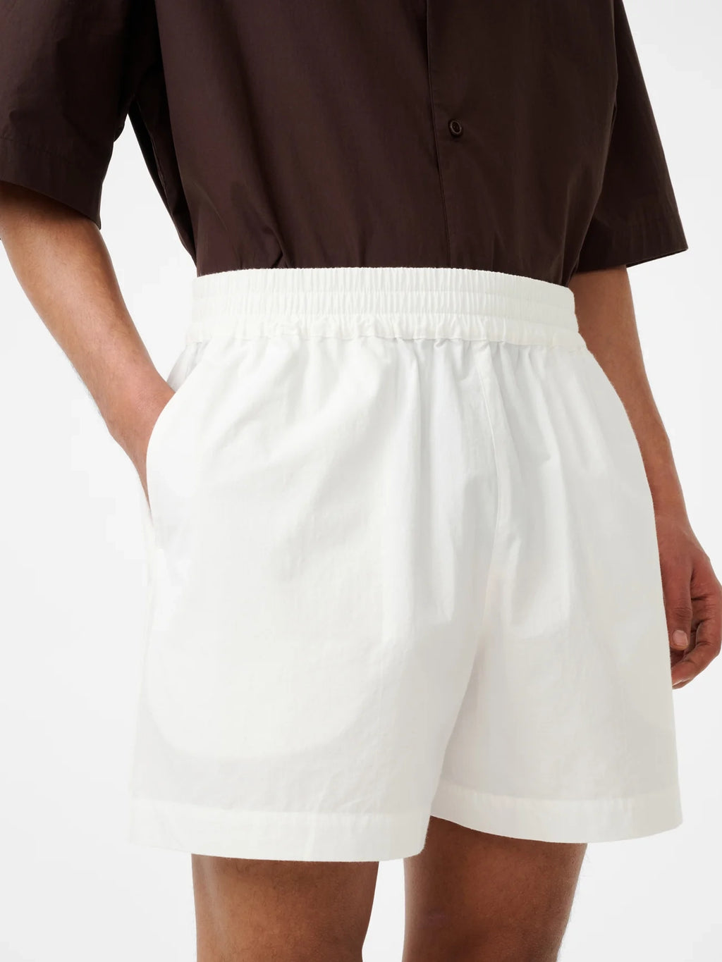 Person wearing white shorts and a brown shirt on a plain background