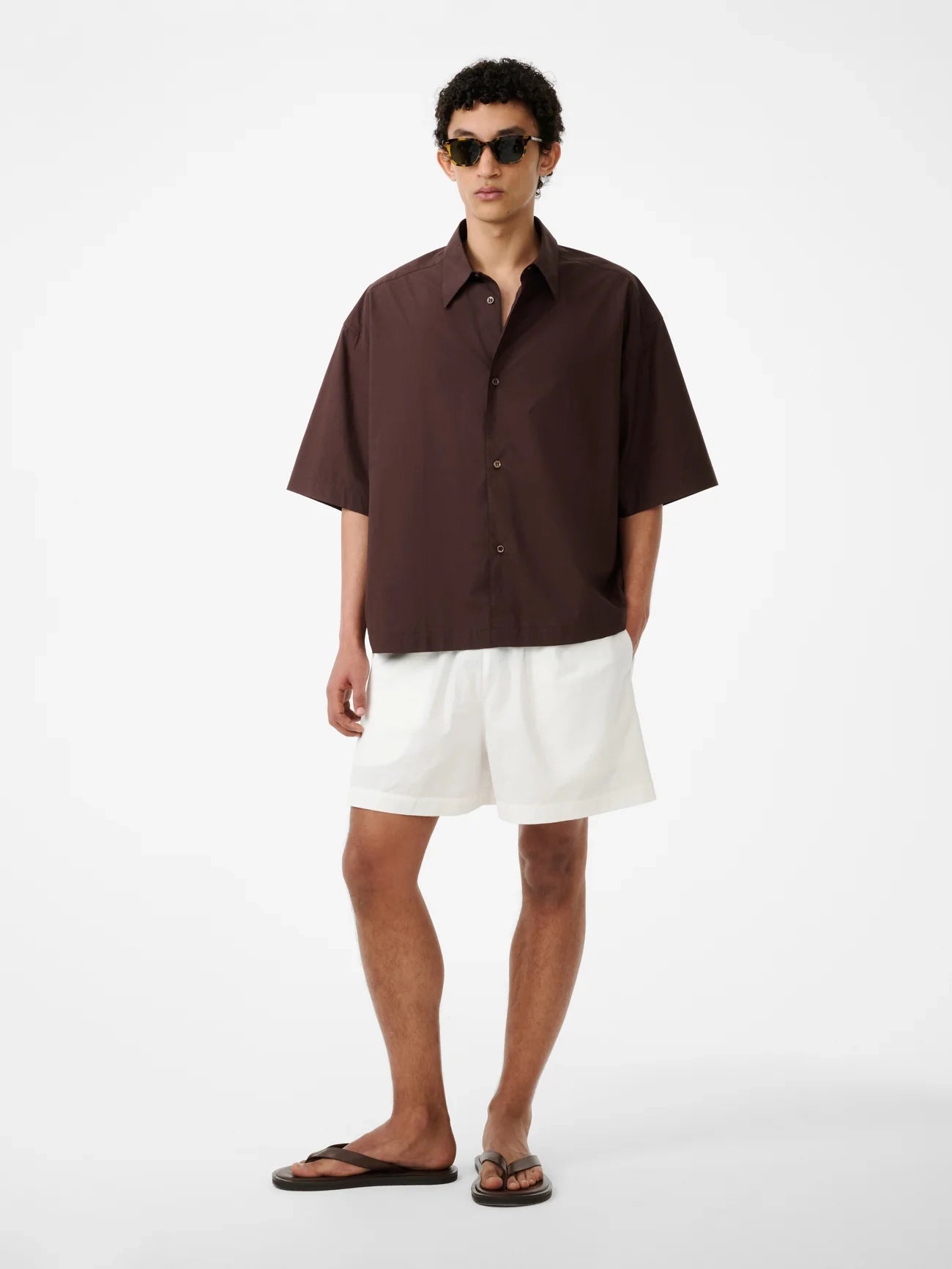 Man wearing a brown shirt and white shorts on a white background