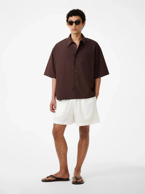Man wearing a brown shirt and white shorts on a white background