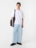 Person wearing a white t-shirt and light blue pants holding a black bag on a white background
