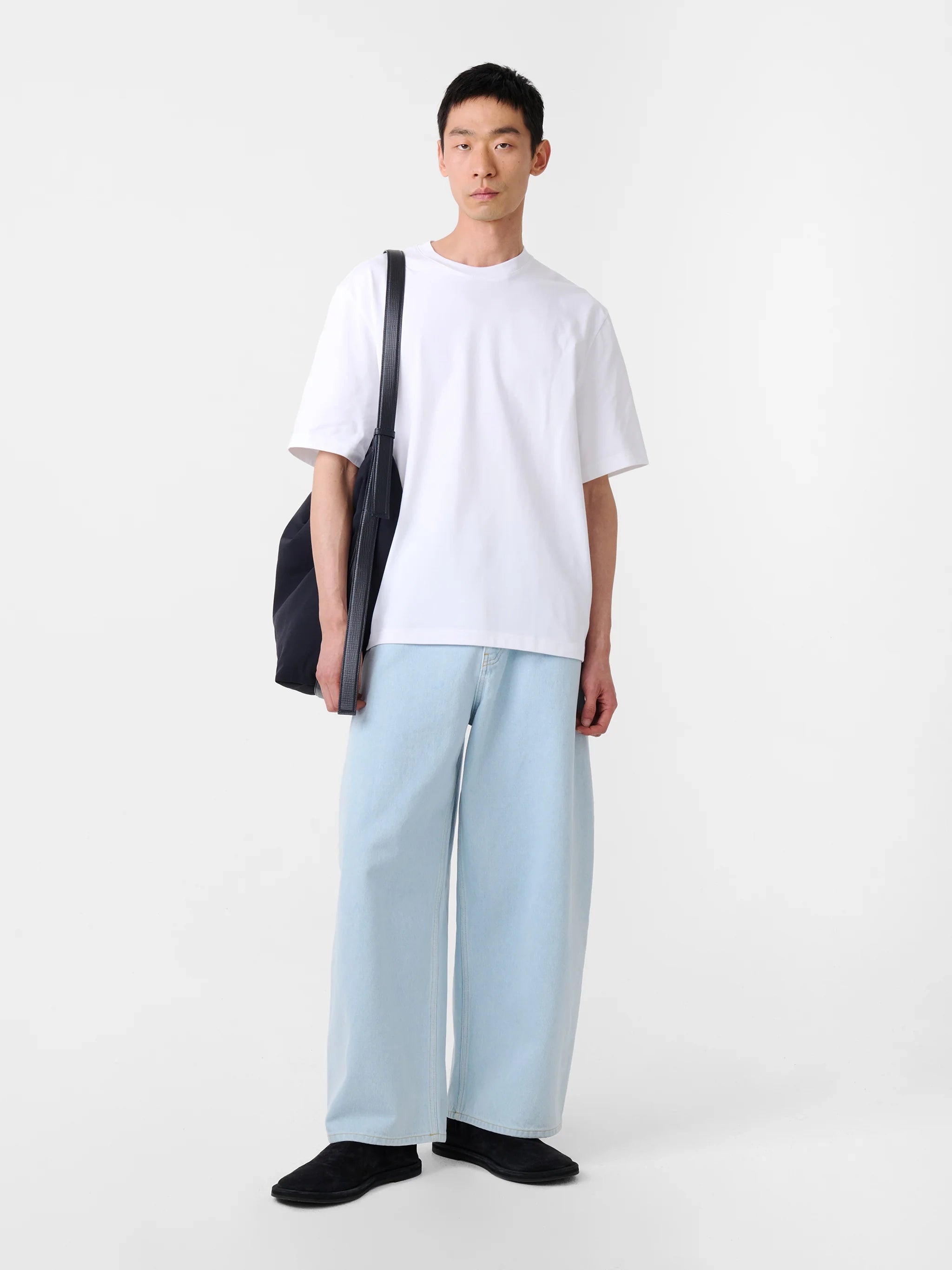 Person wearing a white t-shirt and light blue pants holding a black bag on a white background
