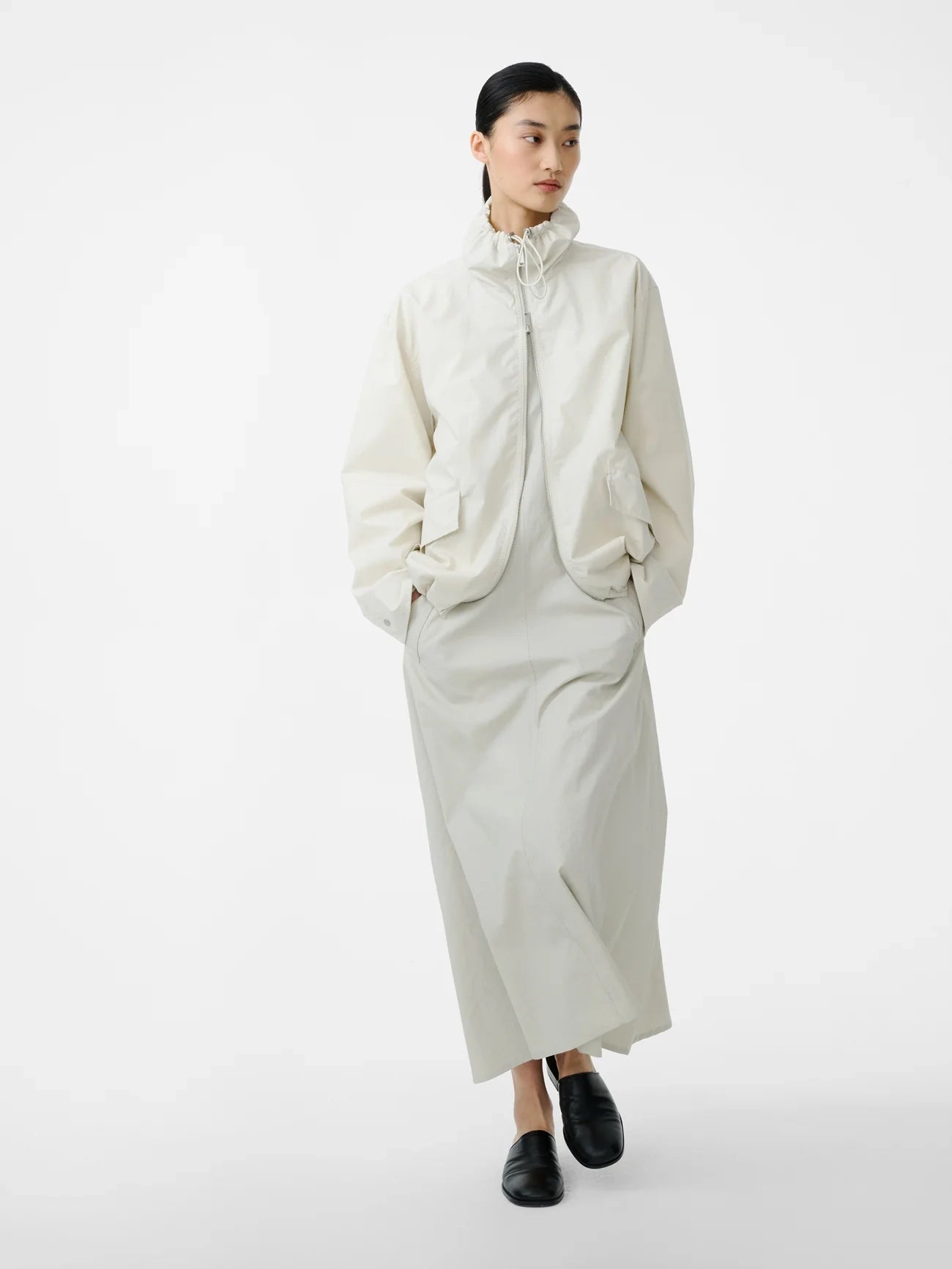 Person wearing a long cream coat on a white background