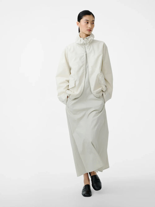 Person wearing a long cream coat on a white background