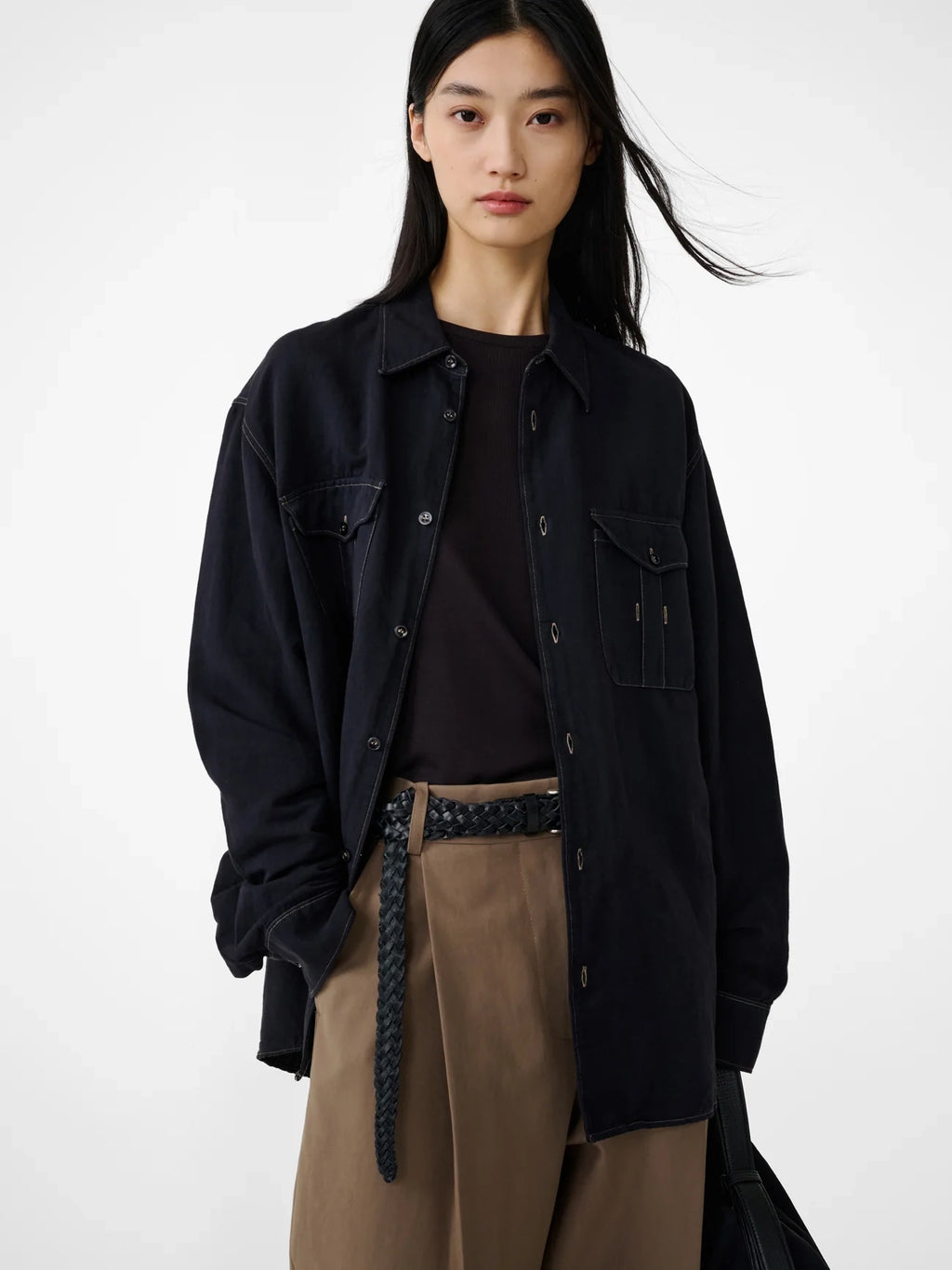 Person wearing a black jacket over a black shirt with brown pants on a white background