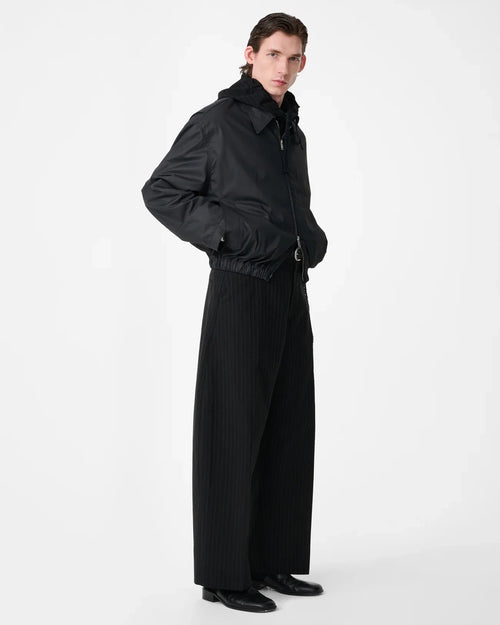 Model wearing Studio Nicholson Lyons black resinated cotton jacket with a classic collar, two-way zip front and elasticated hem.