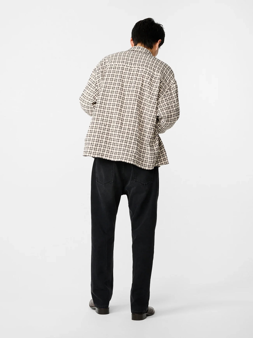 Person wearing a plaid shirt and dark pants on a white background