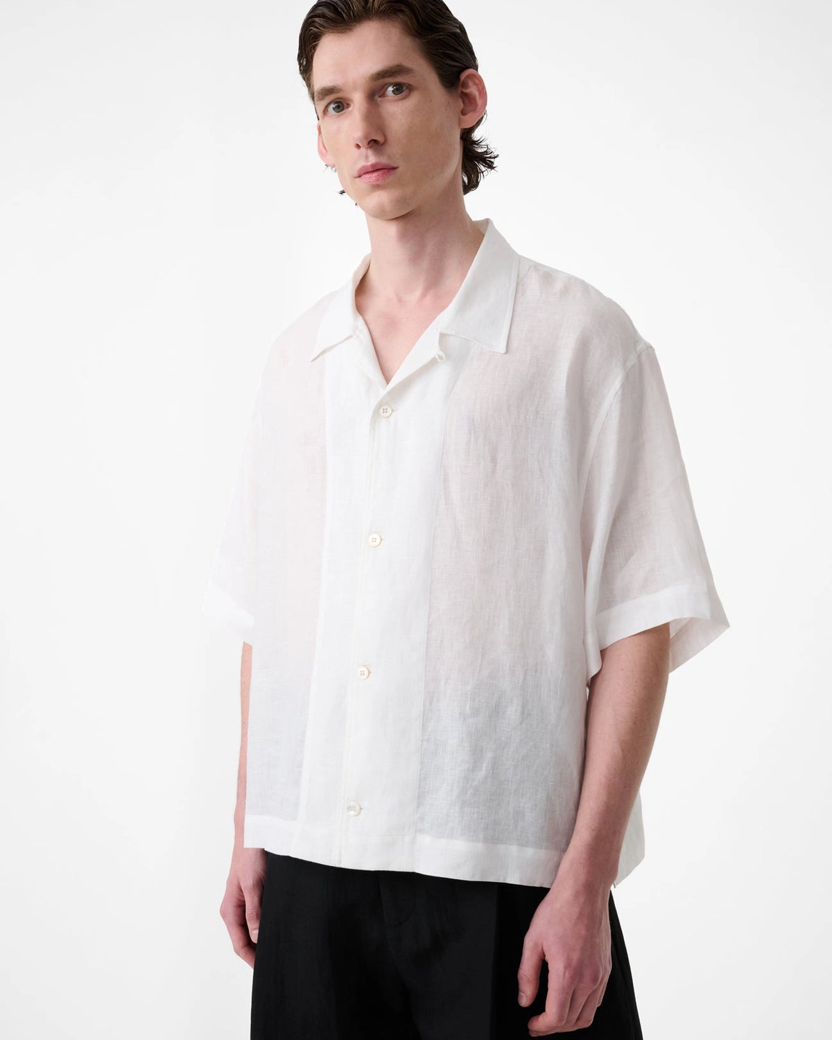 Model wearing Studio Nicholson Oryn white linen short sleeve shirt with a camp collar and straight hem.