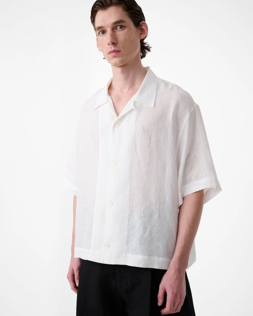 Model wearing Studio Nicholson Oryn white linen short sleeve shirt with a camp collar and straight hem.