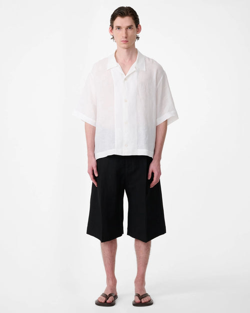 Model wearing Studio Nicholson Oryn white linen short sleeve shirt with a camp collar and straight hem.