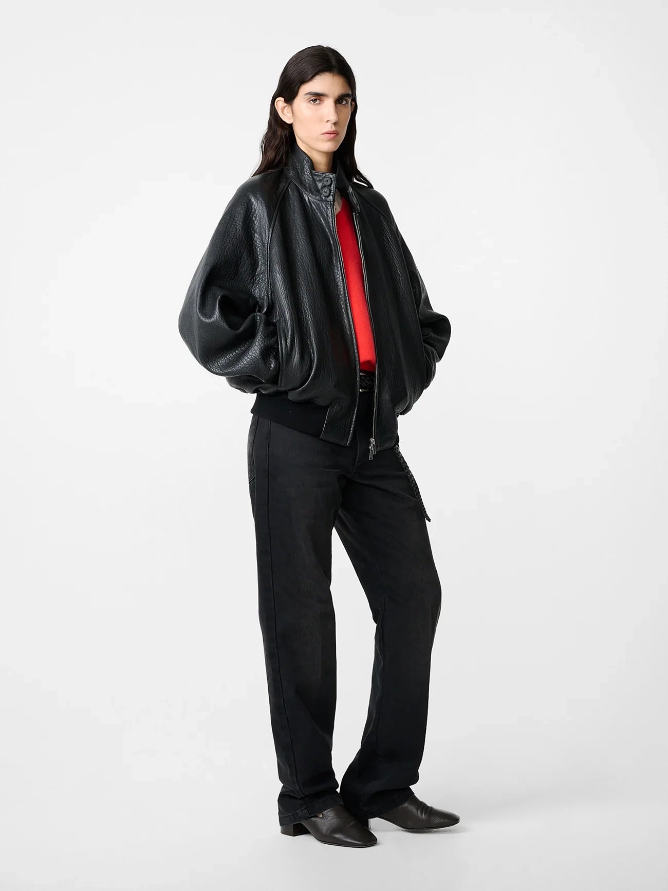 Person wearing a black leather jacket, black shirt with red trim, and black pants on a white background