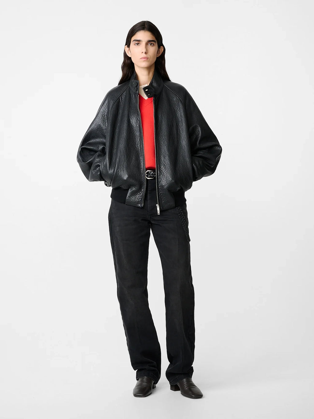 Person wearing a black leather jacket, red shirt, and black pants on a white background