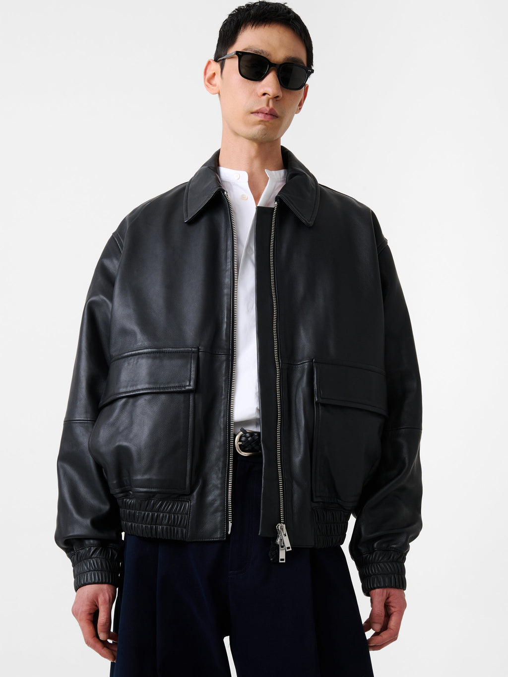 Person wearing a black leather jacket and sunglasses on a white background