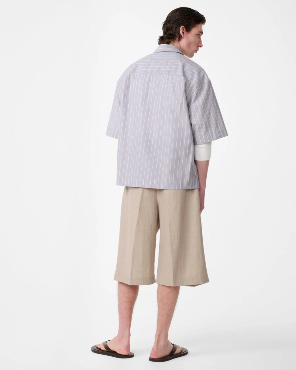 Model wearing Studio Nicholson Sanko short sleeve shirt in grey and brown striped cotton with an oversized fit, point collar and button front.