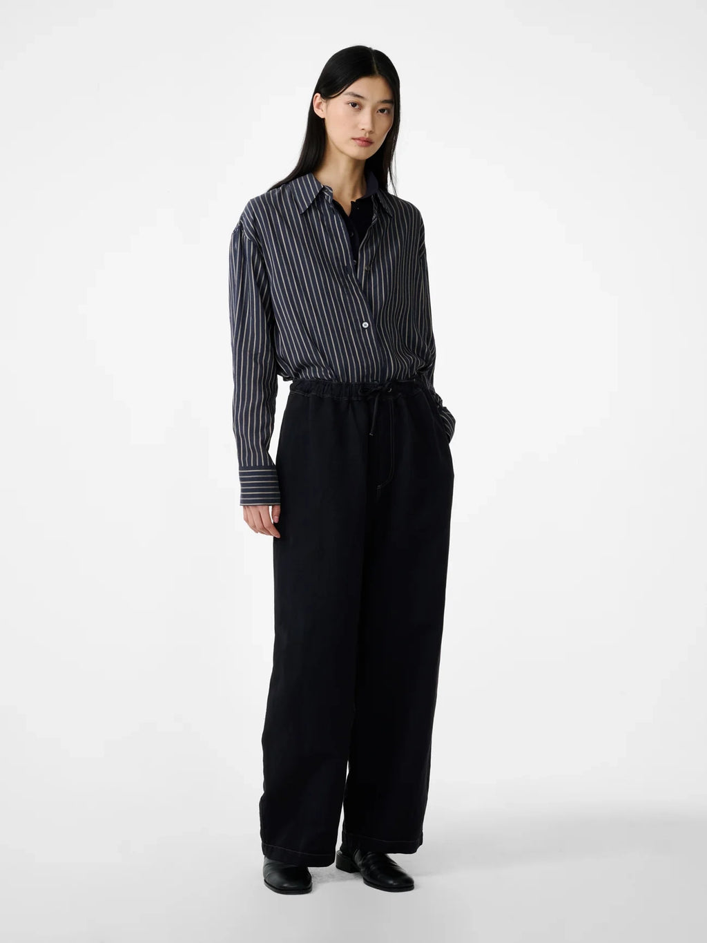 Person wearing a black and white striped shirt with black pants on a white background