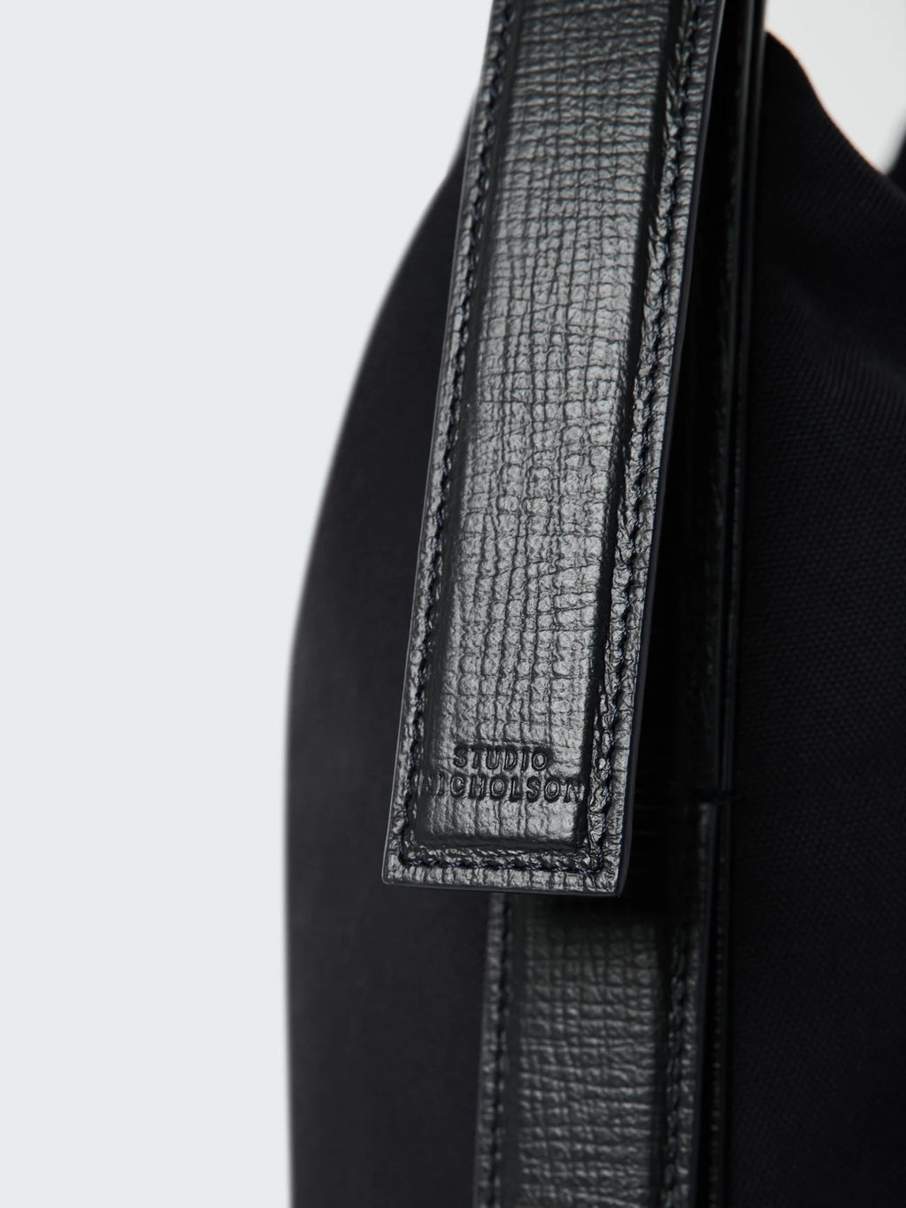 Close-up of a black bag with a textured strap on a light gray background