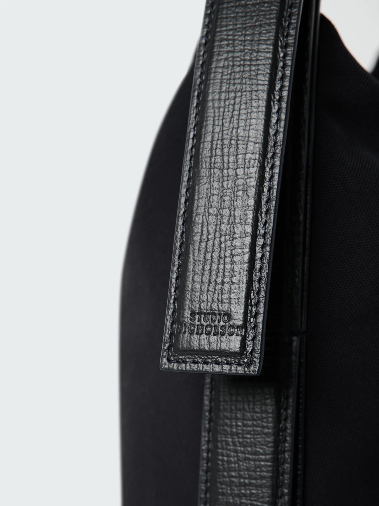 Close-up of a black bag with a textured strap on a light gray background