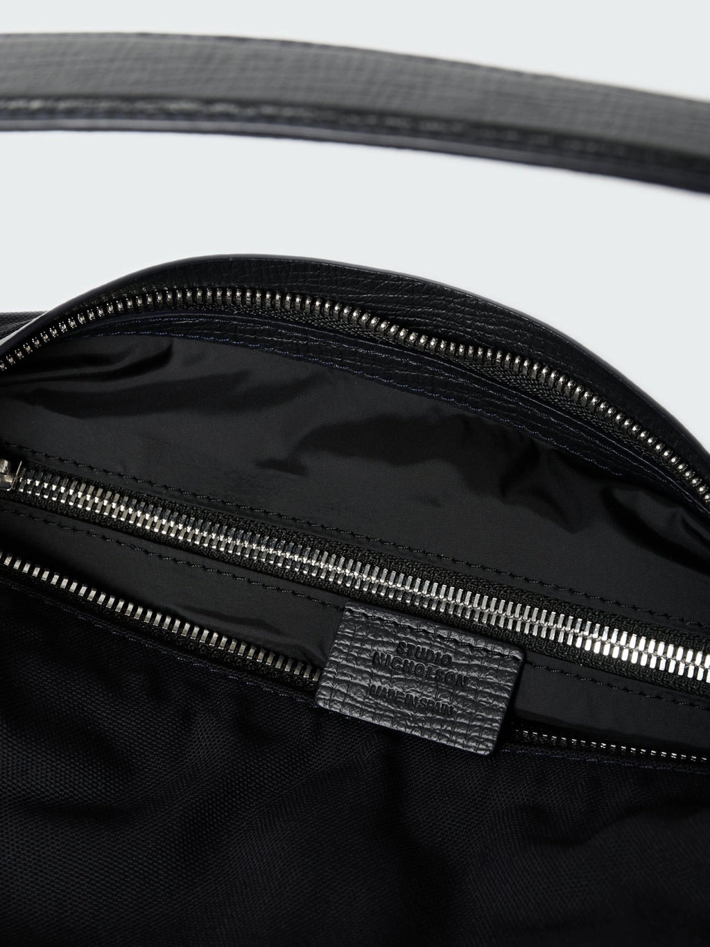 Close-up of a black bag with a zipper and visible brand logo on a white background