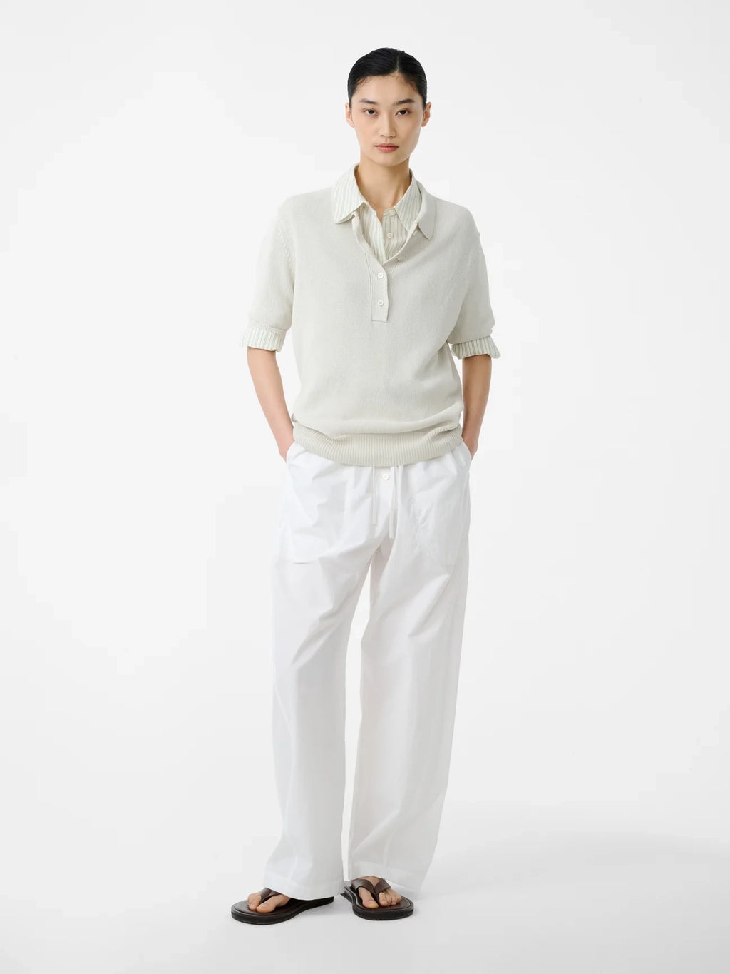 Person wearing a light-colored sweater and white pants on a white background