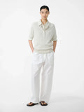 Person wearing a light-colored sweater and white pants on a white background