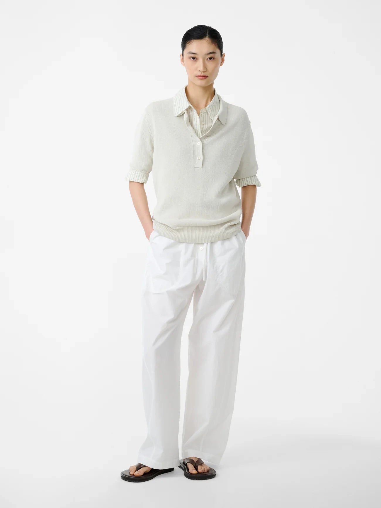 Person wearing a light-colored sweater and white pants on a white background