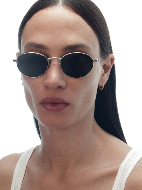 Model wearing THISTLES CRUZ sunglasses in silver titanium with an oval wire frame silhouette and dark green G15 lenses.
