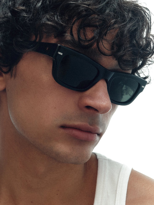 Model wearing THISTLES JACK sunglasses in black acetate with an angular wayfarer-inspired silhouette and dark green G15 lenses.