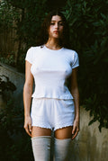 A woman wearing a white short-sleeved cotton top and matching shorts, standing outdoors.